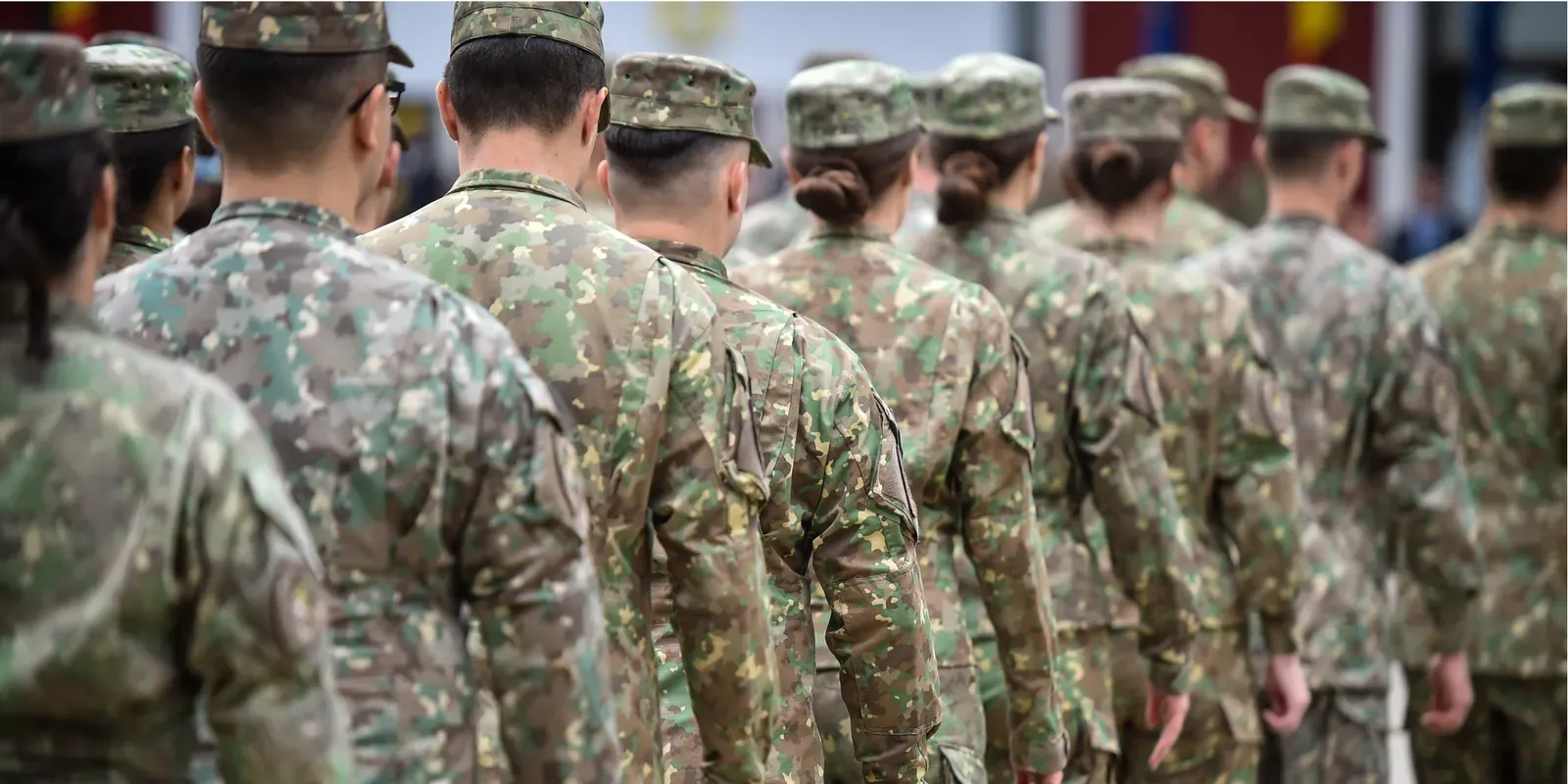 Service members in camouflage uniforms standing in formation, seen from behind